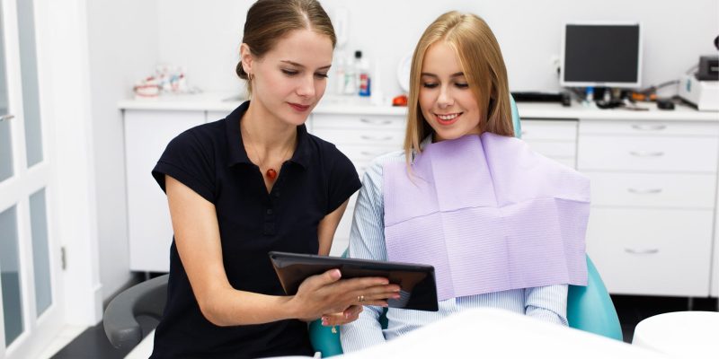 Smiling woman sits in the chair at dentist office while doctor shows her something